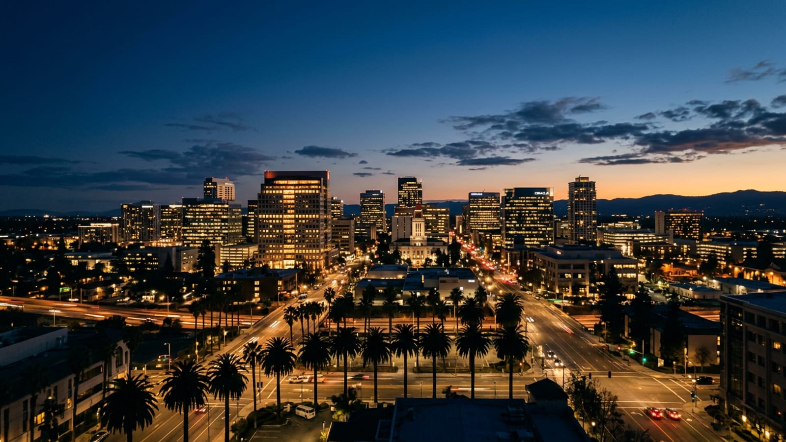 Downtown San Jose at blue hour with lit office towers and silhouetted palm trees under a deep navy sky